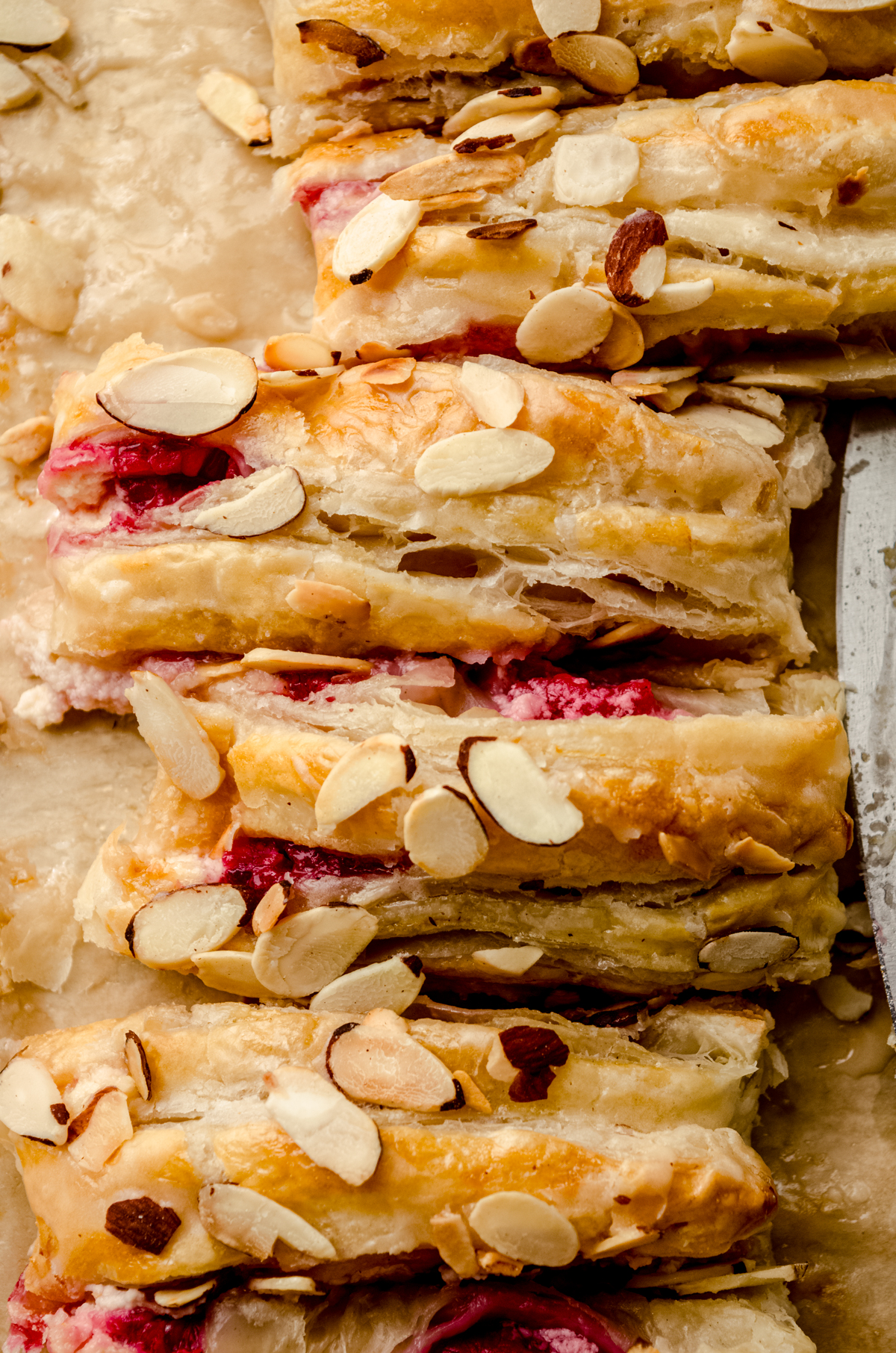 A pastry braid filled with raspberries and cream cheese with toasted almonds and an icing on it sliced into portions.