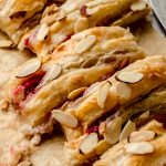 A pastry braid filled with raspberries and cream cheese with toasted almonds and an icing on it sliced into portions.