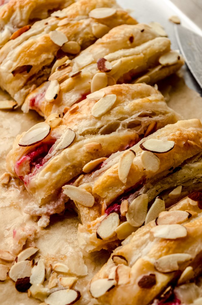 A pastry braid filled with raspberries and cream cheese with toasted almonds and an icing on it sliced into portions.