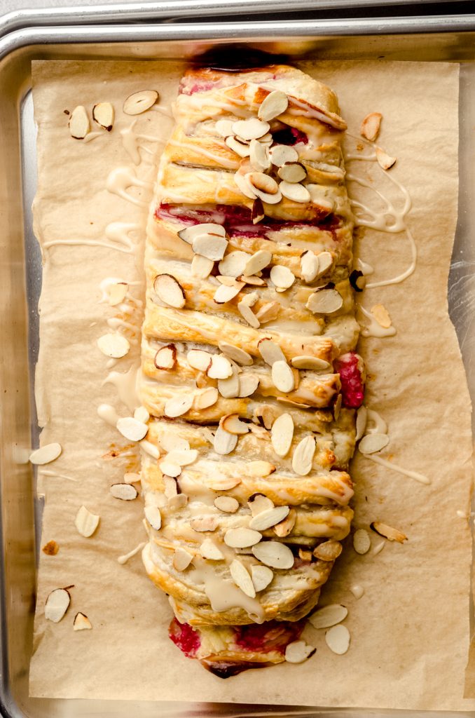 A pastry braid filled with raspberries and cream cheese with toasted almonds and an icing on it.