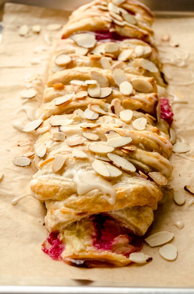 A pastry braid filled with raspberries and cream cheese with toasted almonds and an icing on it.