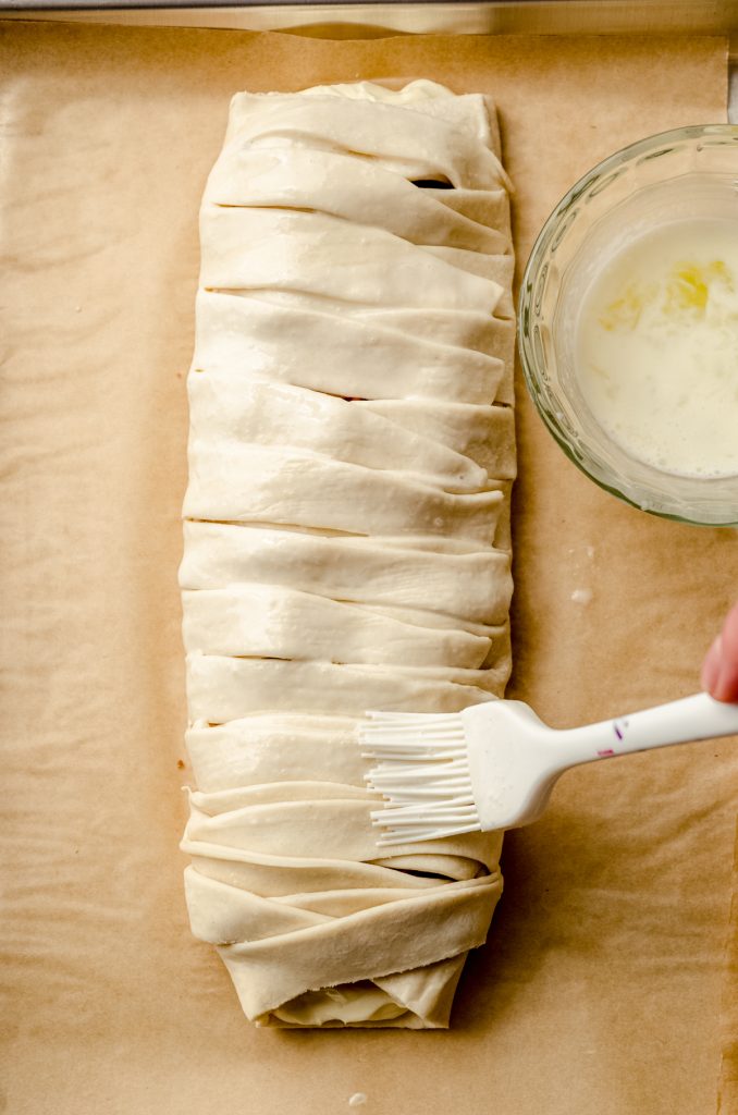 Someone is brushing a pastry braid with an egg wash.