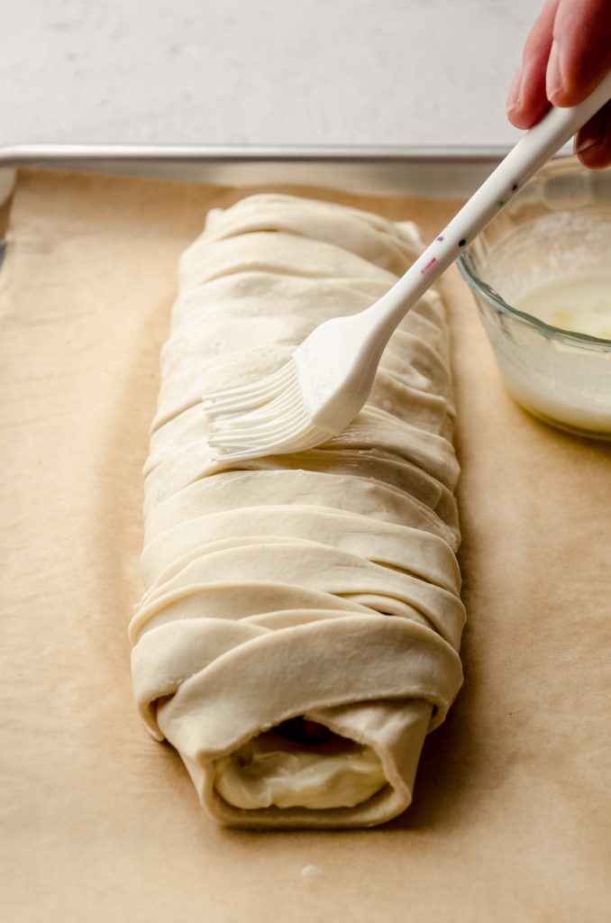 Someone is brushing a pastry braid with an egg wash.