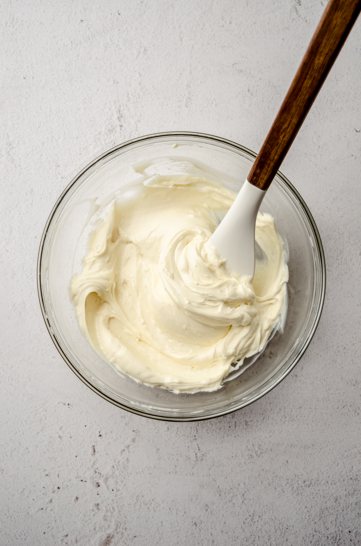 A bowl of cream cheese filling for raspberry cream cheese danish with a spatula in it.