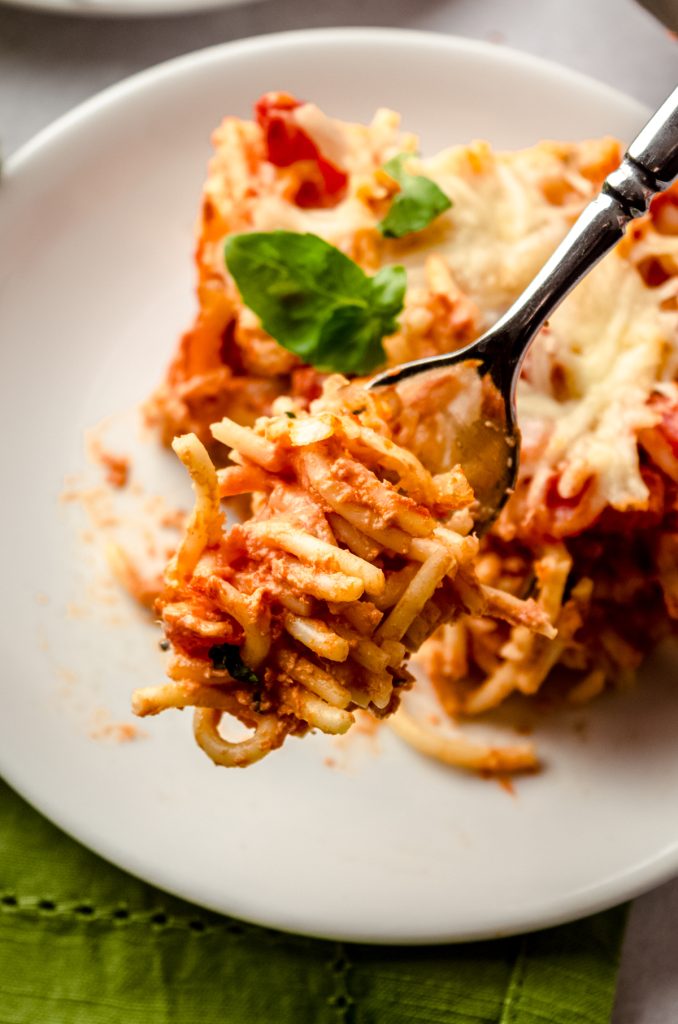 A fork full of spaghetti casserole and you can see the slice of casserole on a dish in the background.