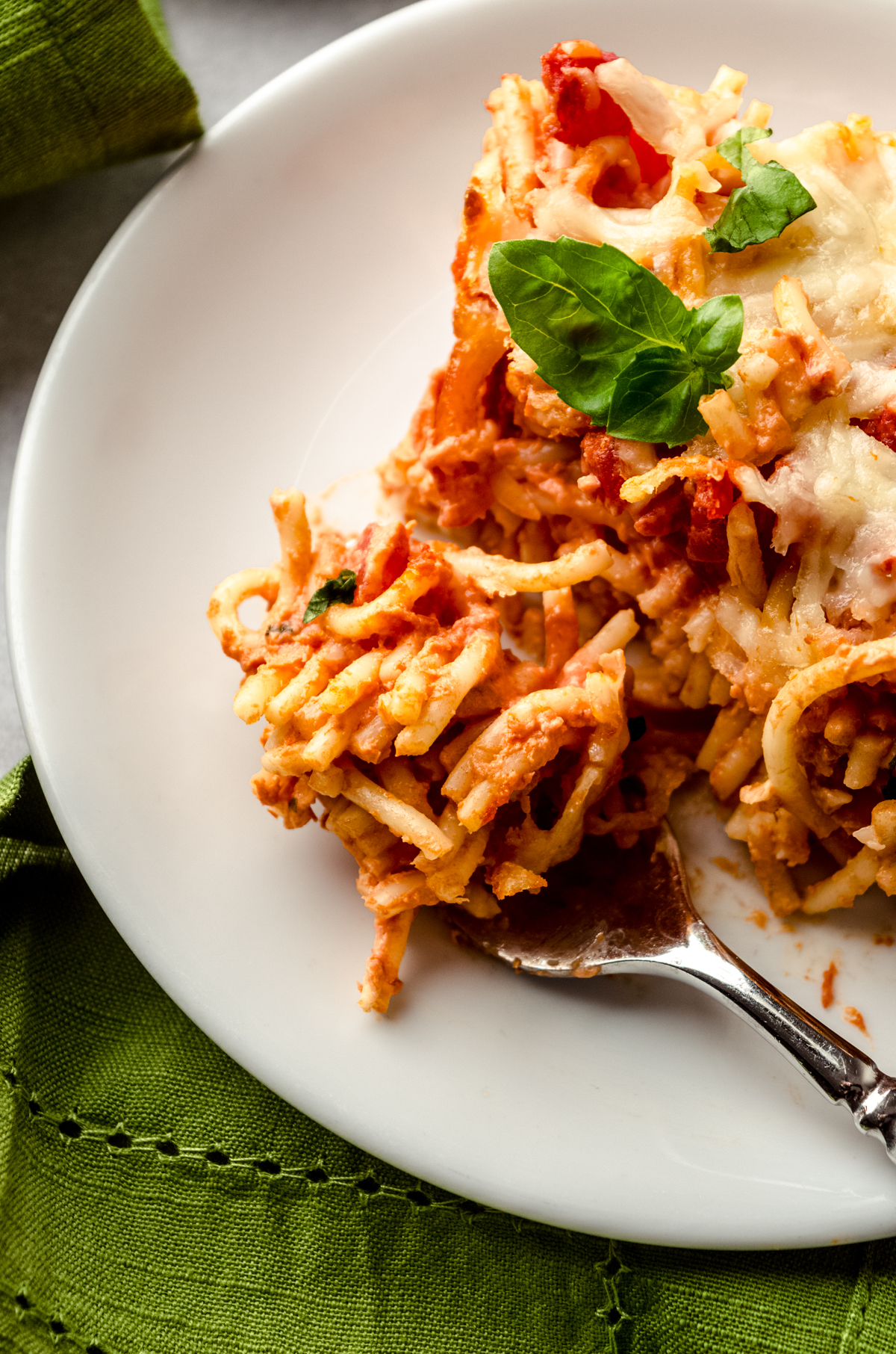 A fork on a plate with a bite of spaghetti casserole on it sitting next to the slice of casserole.