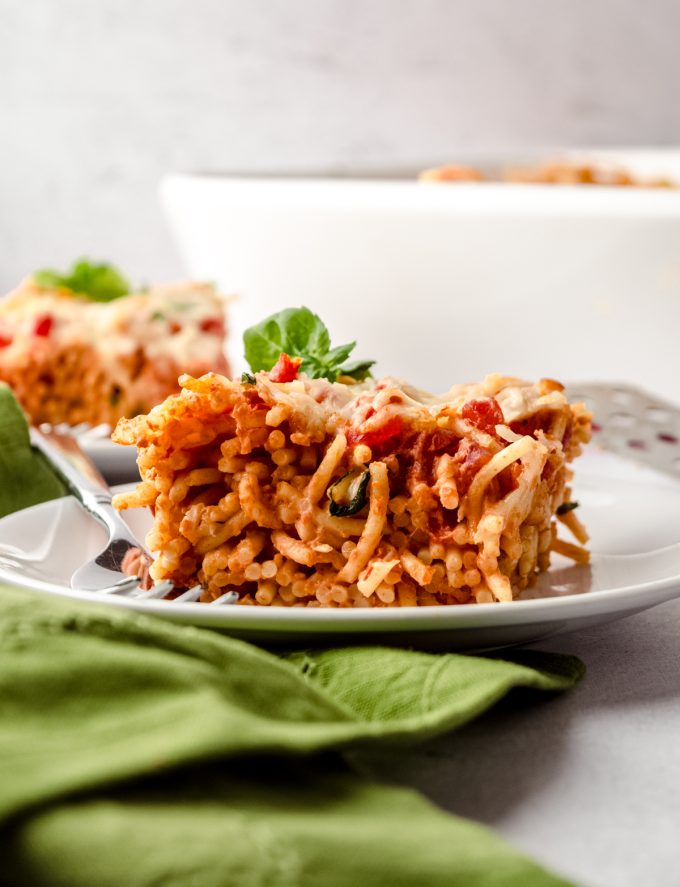 A slice of baked cream cheese spaghetti casserole on a plate with a fork.