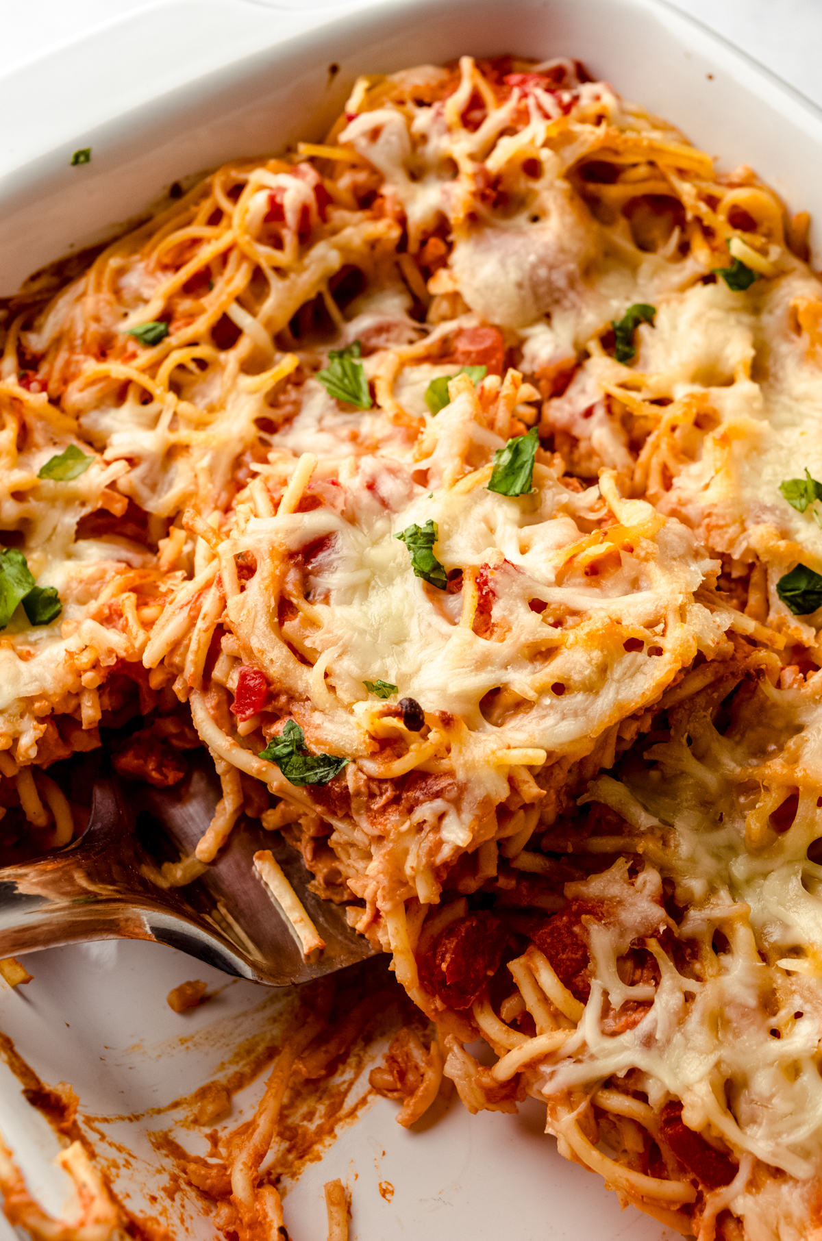 Someone is lifting a slice of baked cream cheese spaghetti casserole out of a baking dish.