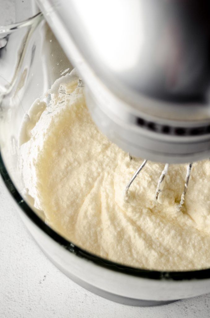 A curdling Swiss meringue buttercream mixture in the bowl of a stand mixer fitted with the whisk attachment.