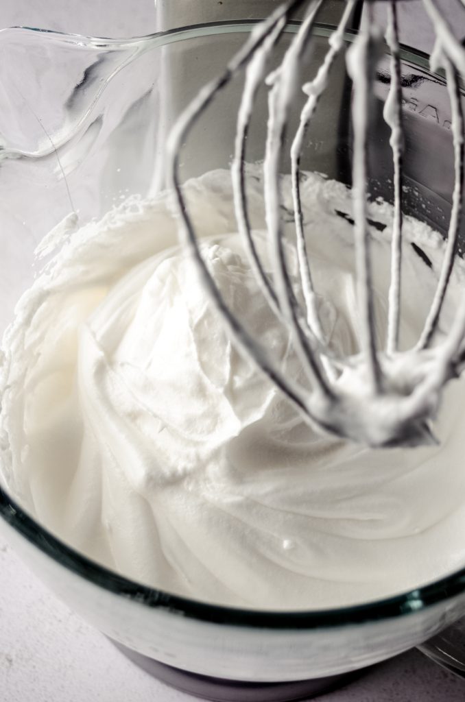 Stiff peaks in the bowl of a stand mixer fitted with the whisk attachment whipping meringue.