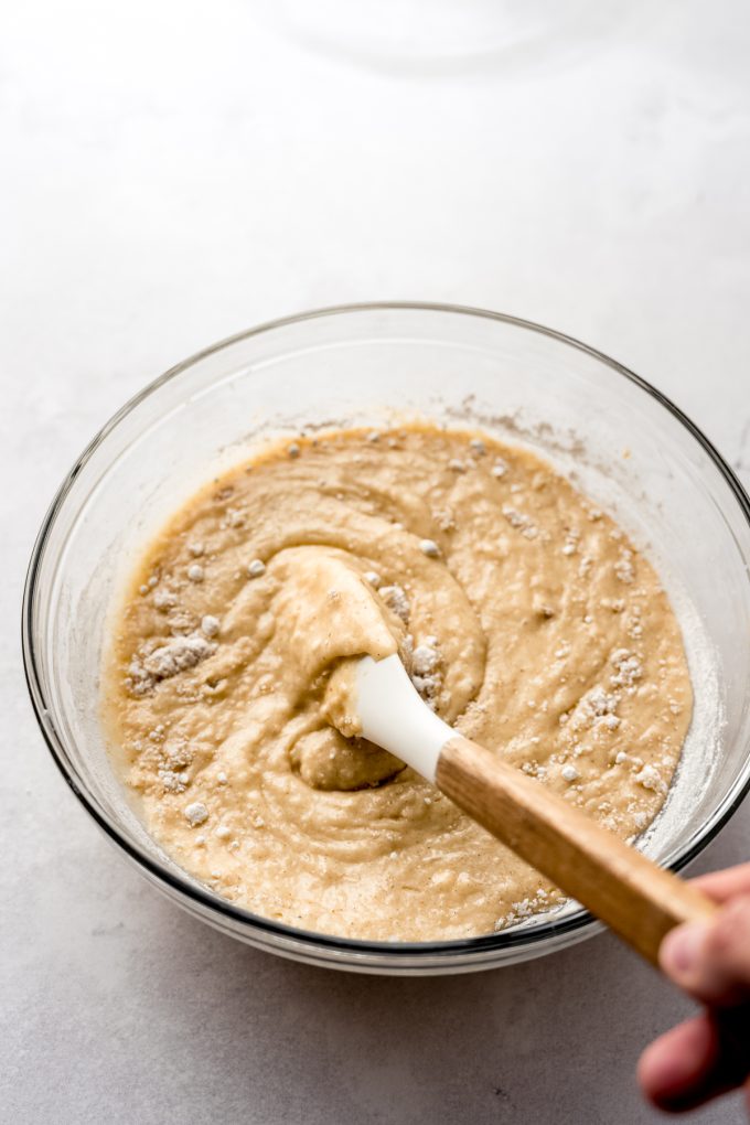 Aerial photo of someone using a spatula to stir banana bread batter in a large bowl.