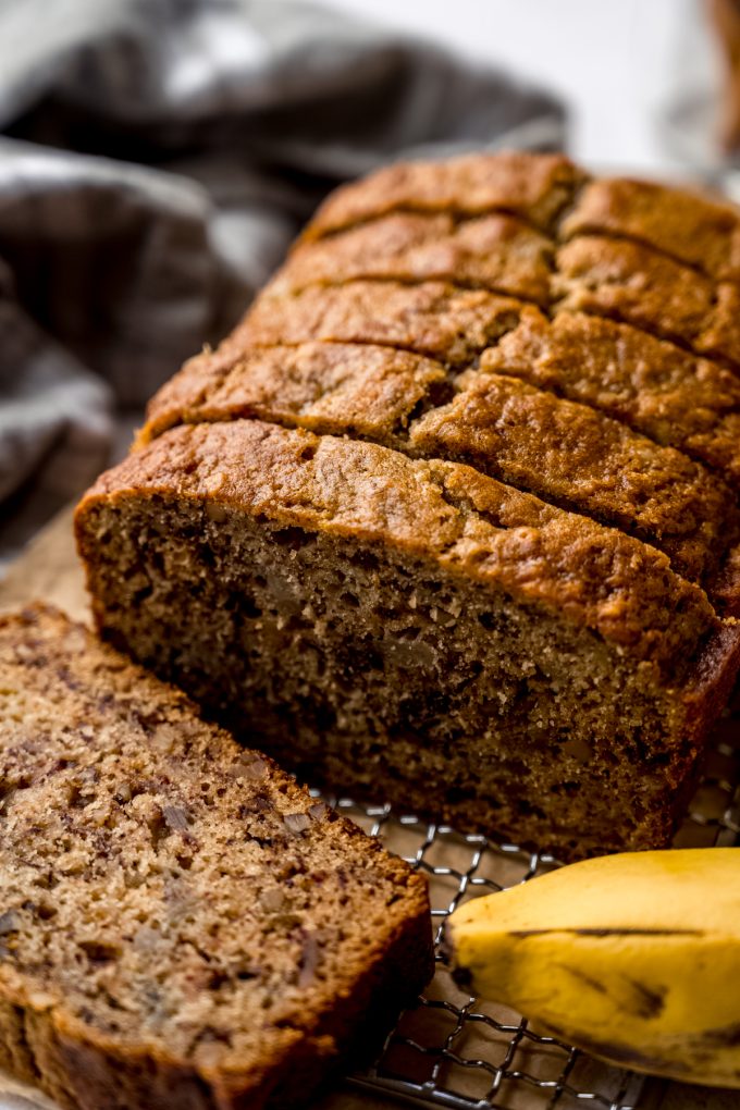 A loaf of banana bread made with unripe bananas that has been sliced and sitting on a cooling rack.