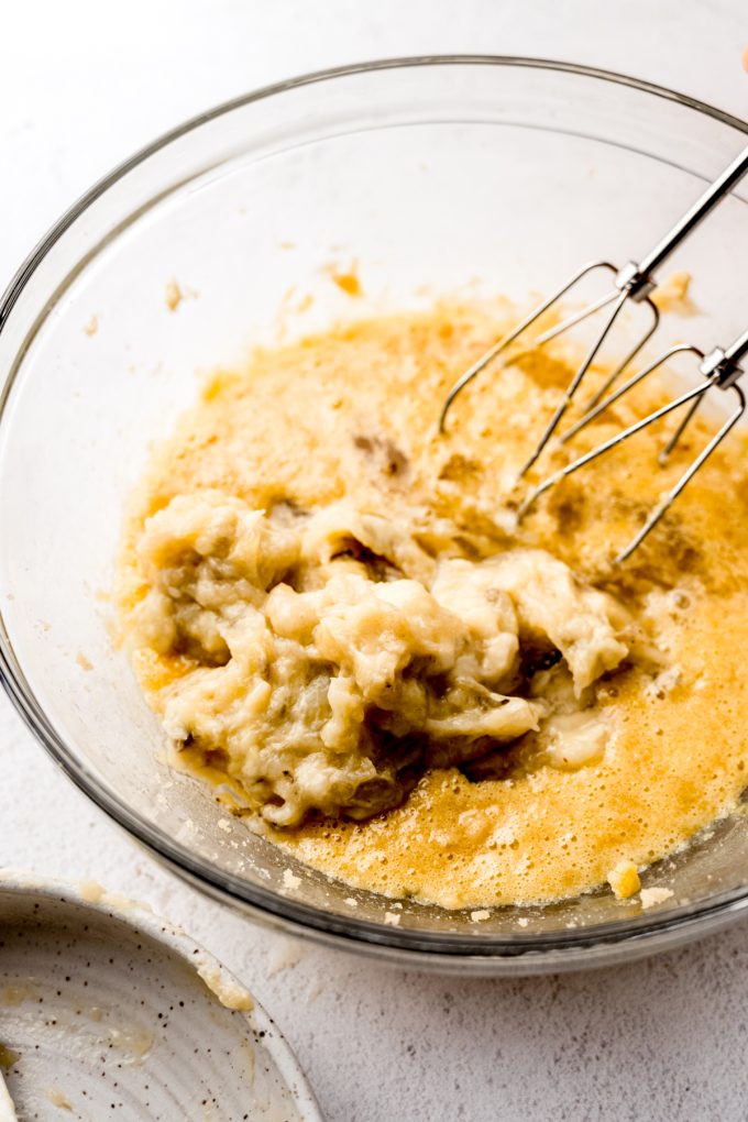 Banana bread batter coming together in a bowl with electric beaters.