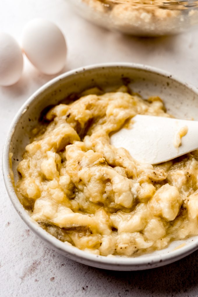 Mashed roasted bananas in a white bowl with a spatula.