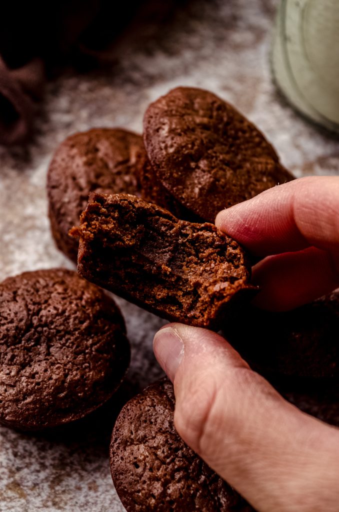 Fingers holding a brownie bite that has a bite taken out of it.