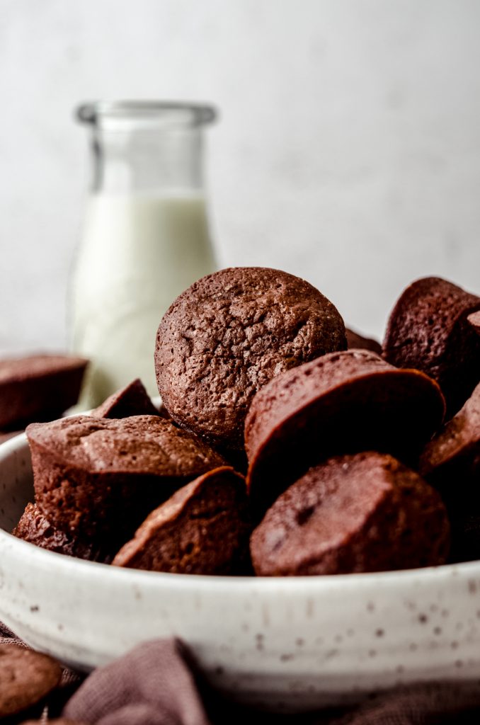 A bowl of brownie bites with a bottle of milk in the background.