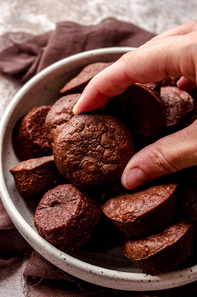 Someone is holding a brownie bite over a bowl of brownie bites.