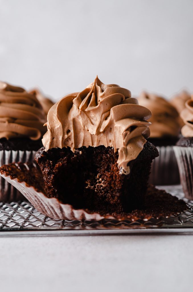 A chocolate cupcake with the wrapper pulled down and a bite taken out of it.