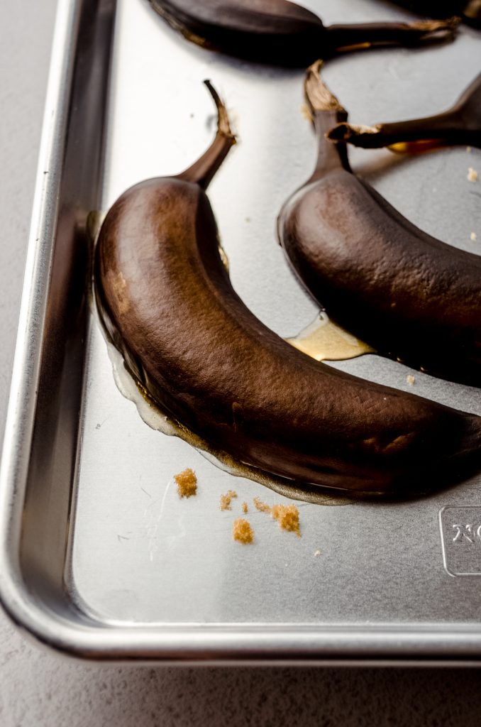 Sliced bananas with the peel still on on a baking sheet that have been sliced open and roasted.