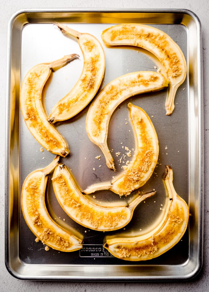 Aerial photo of yellow bananas that have been sliced long ways and sprinkled with brown sugar lying face up on a baking sheet.