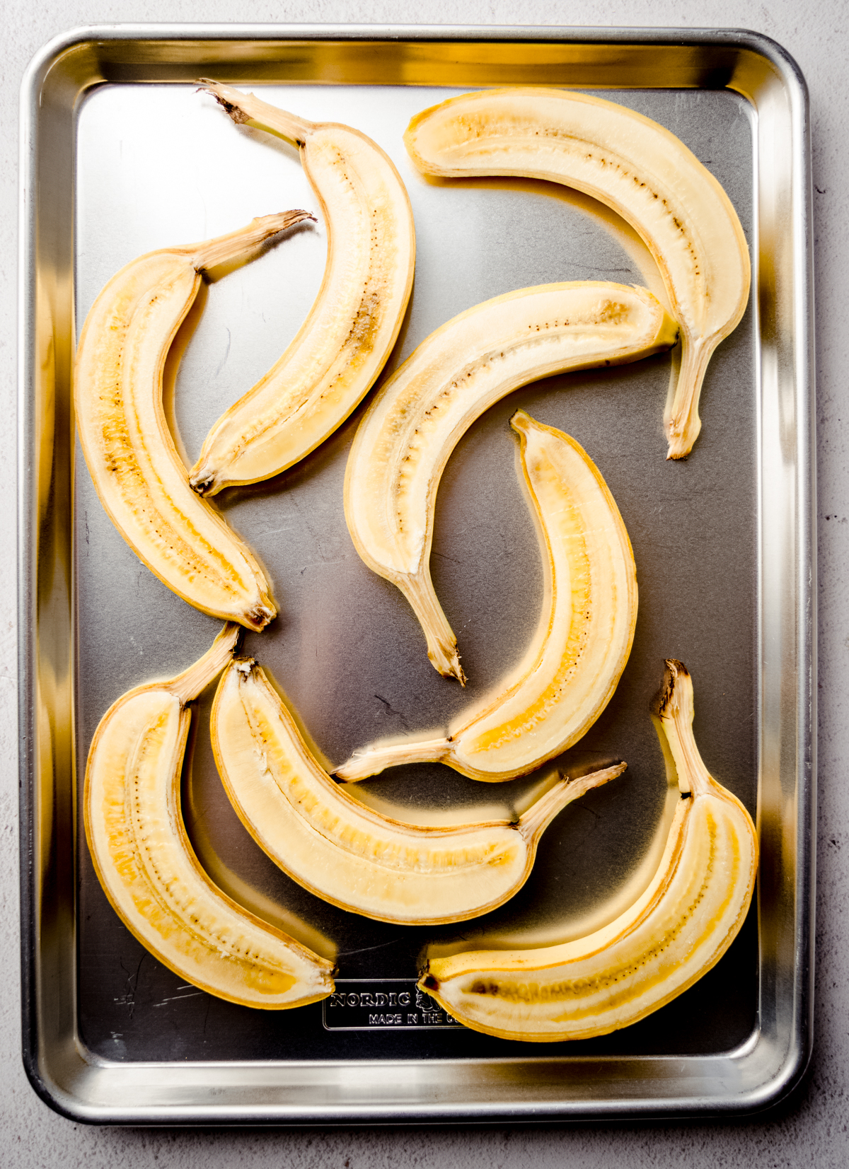 Aerial photo of yellow bananas that have been sliced long ways lying face up on a baking sheet.