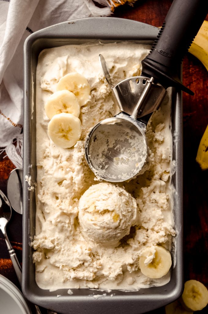 Aerial photo of a loaf pan filled with roasted banana ice cream with an ice cream scoop in it and a scoop of ice cream formed and sitting in the container.