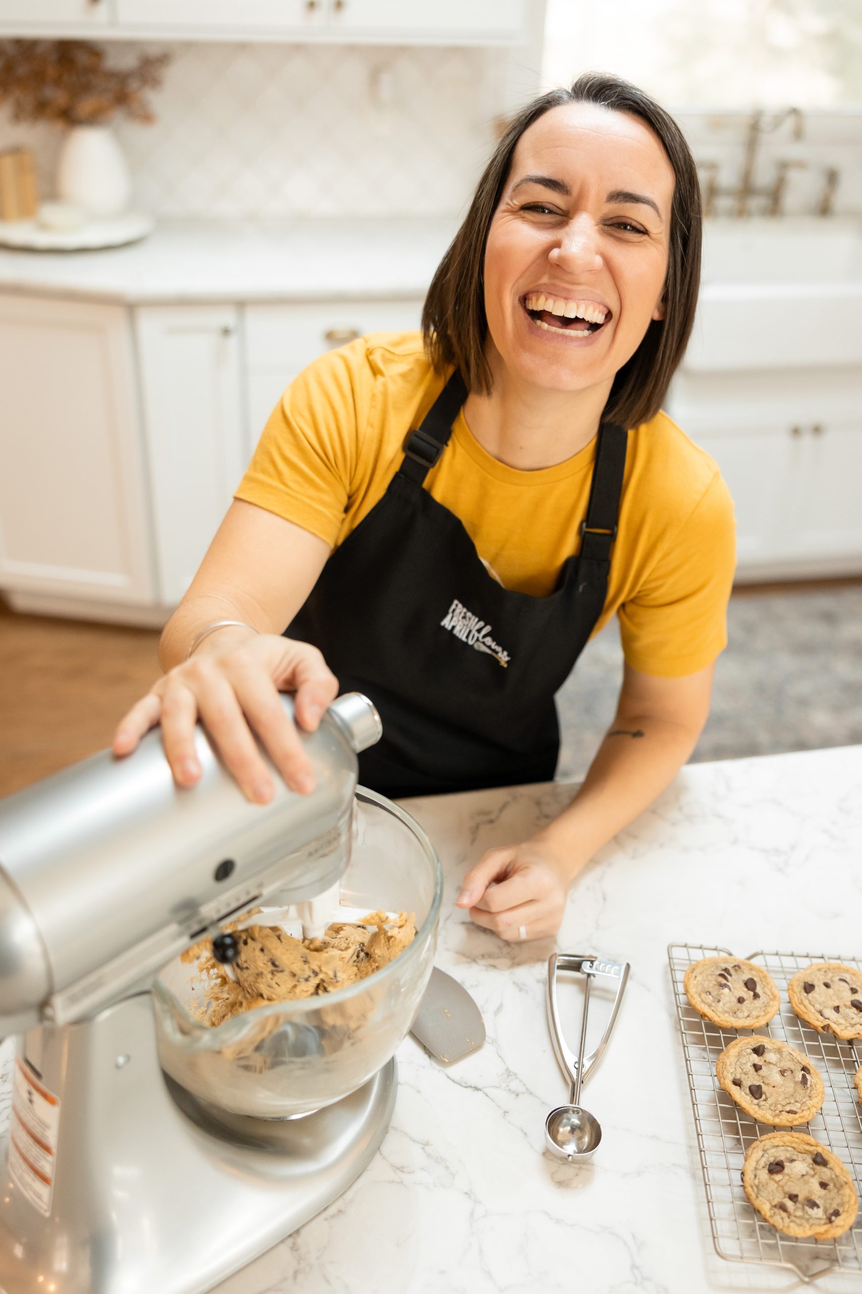 A woman in a kitchen with a mixer and cookies on the counter in front of her.