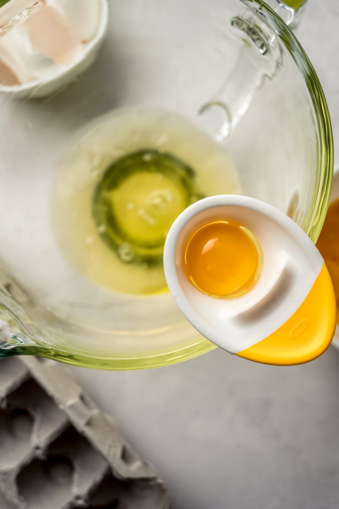 Aerial photo of an egg separator attached to the edge of a large glass mixing bowl with a yolk in it. 