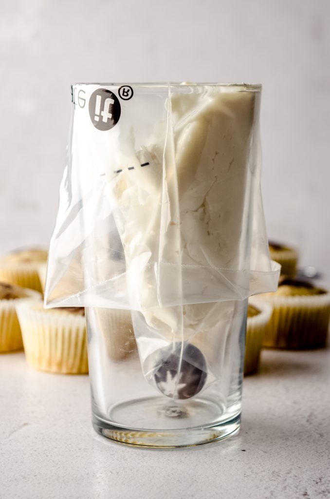 A piping bag fitted with a piping tip and sitting in a tall glass with white frosting in one side of it. 