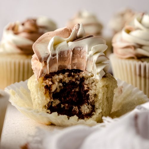 A marble cupcake with a bite taken out of it so you can see the inside of it.