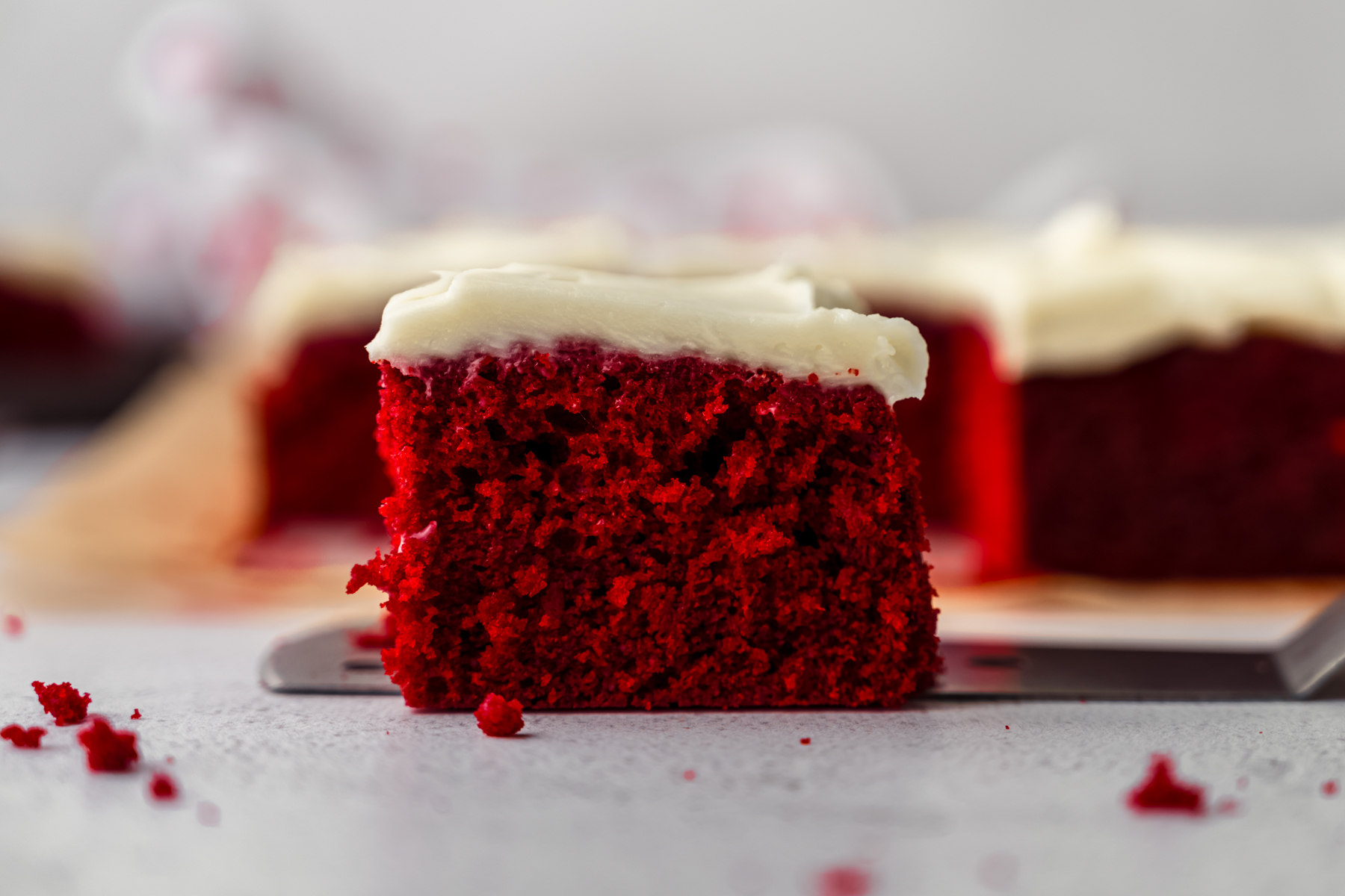 A slice of red velvet sheet cake on a surface sitting on a cake server.