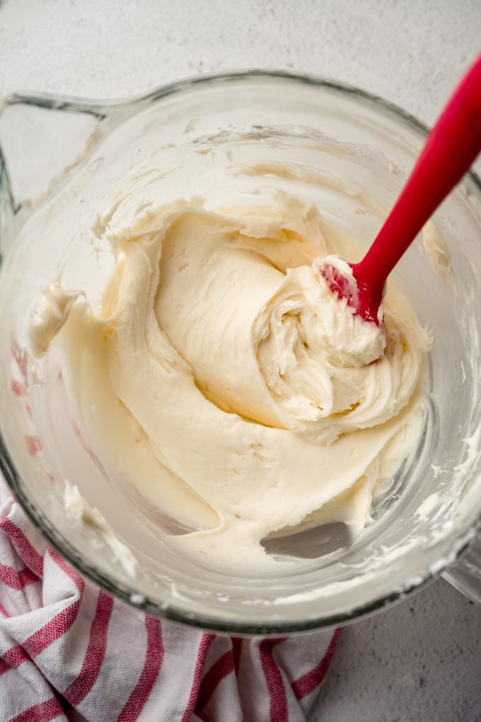 Aerial photo of a bowl of cream cheese frosting with a red spatula in it.