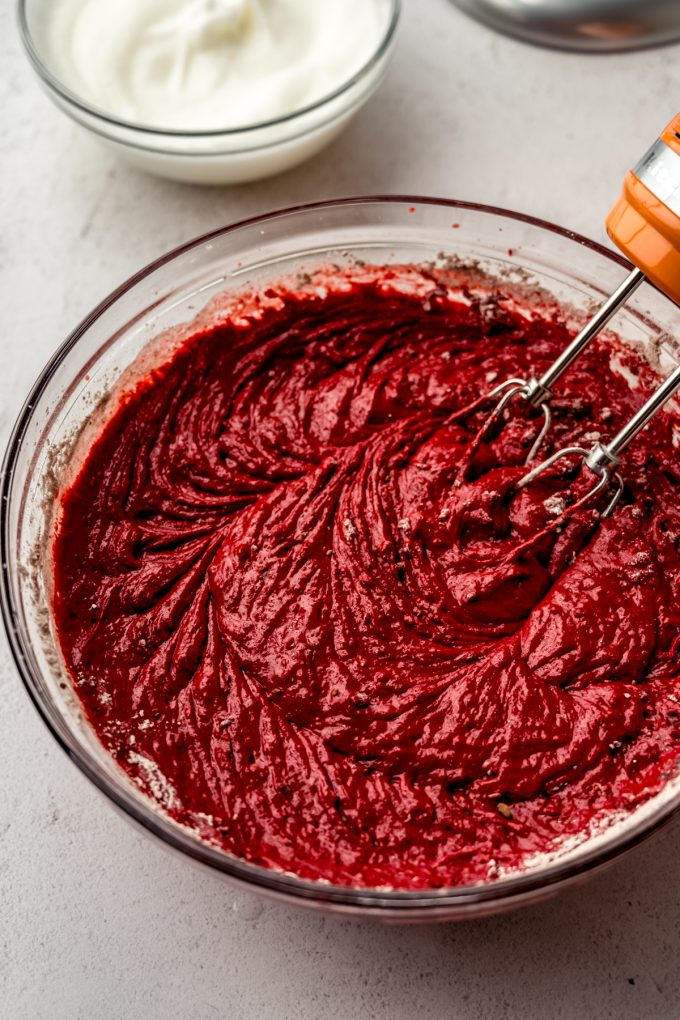 Red velvet cake batter in a bowl with an electric mixer.