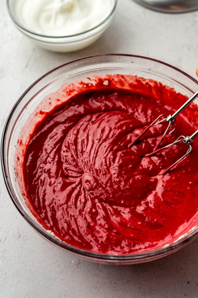 Red velvet cake batter in a bowl with an electric mixer.