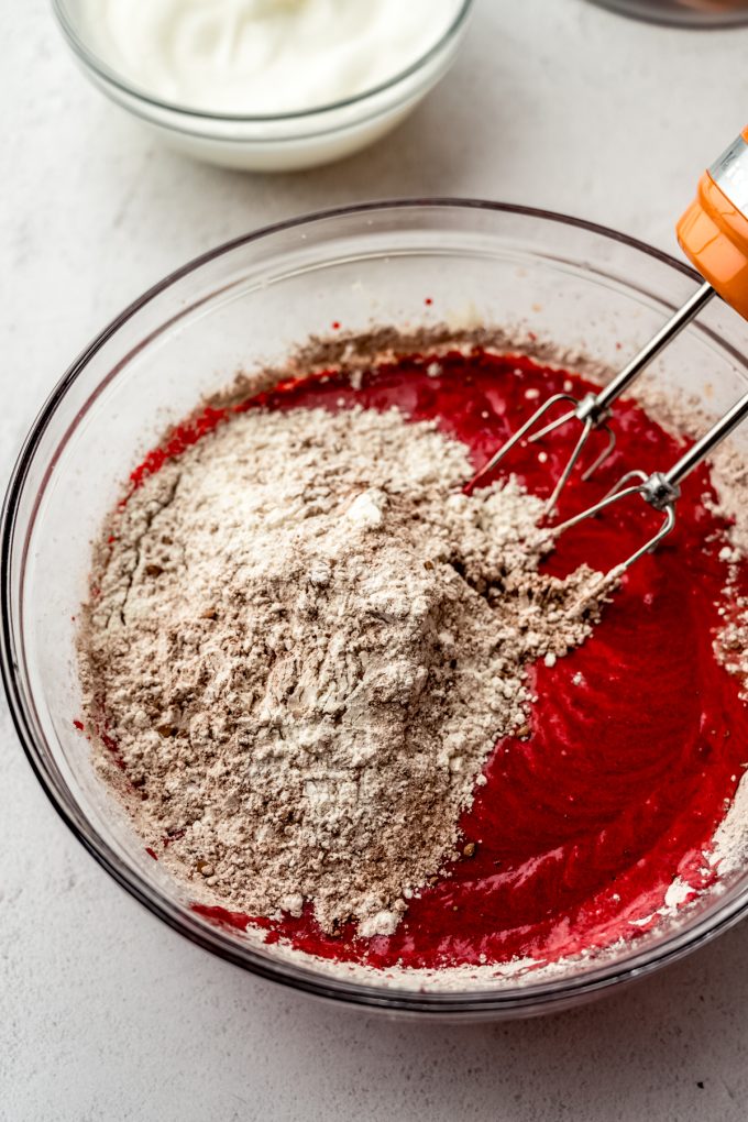 Red velvet cake batter in a bowl with an electric mixer.