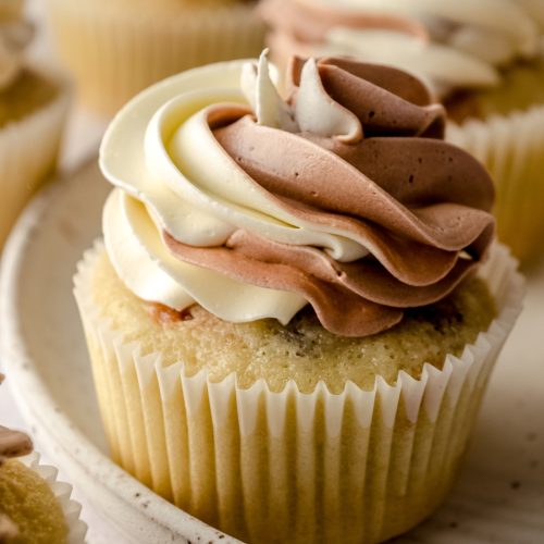 A cupcake with vanilla/chocolate swirled frosting piped on top.