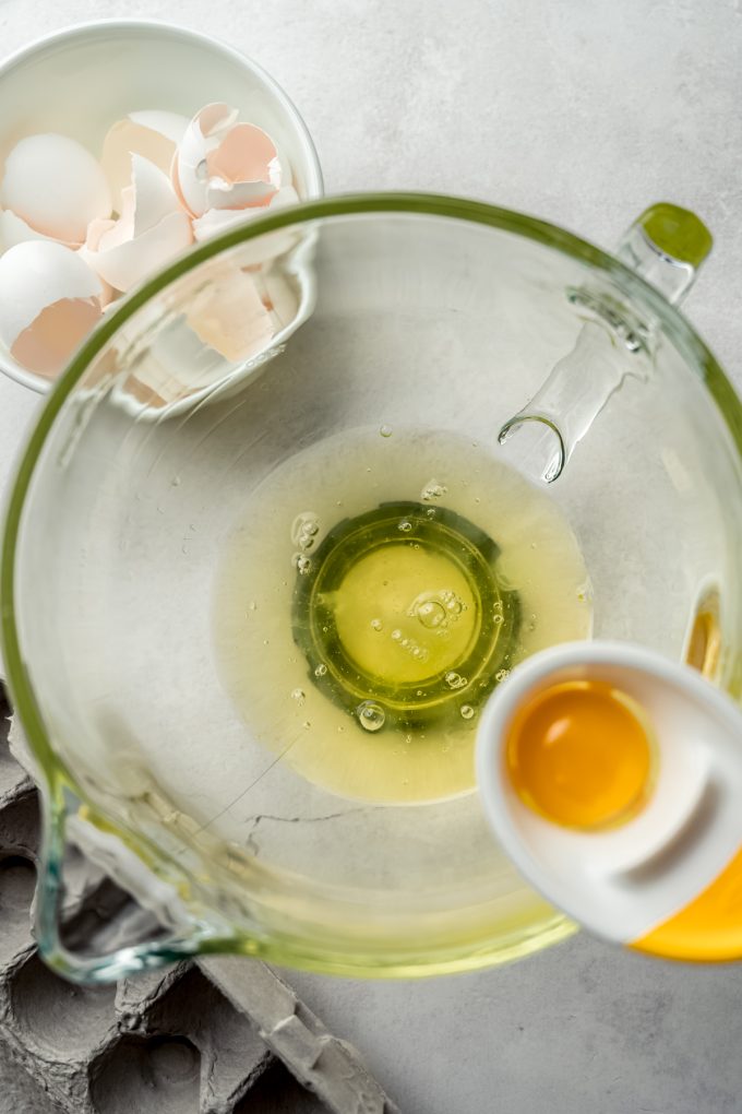 Aerial photo of an egg separator attached to the edge of a bowl of a stand mixer and there is a yolk in the separator and whites in the bowl.