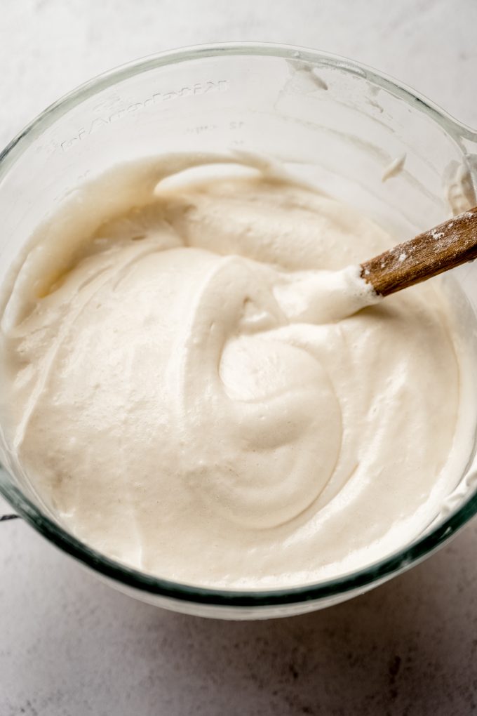 The batter for angel food cake in a large glass bowl with a spatula.