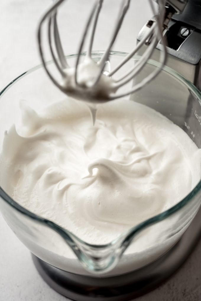 The bowl of a stand mixer fitted with the whisk attachment showing soft peaks in the bowl.