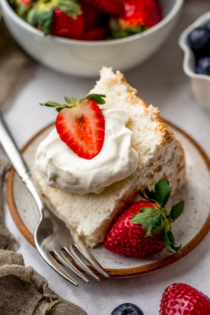 A slice of angel food cake with whipped cream and strawberries on it sitting on a plate with a fork.