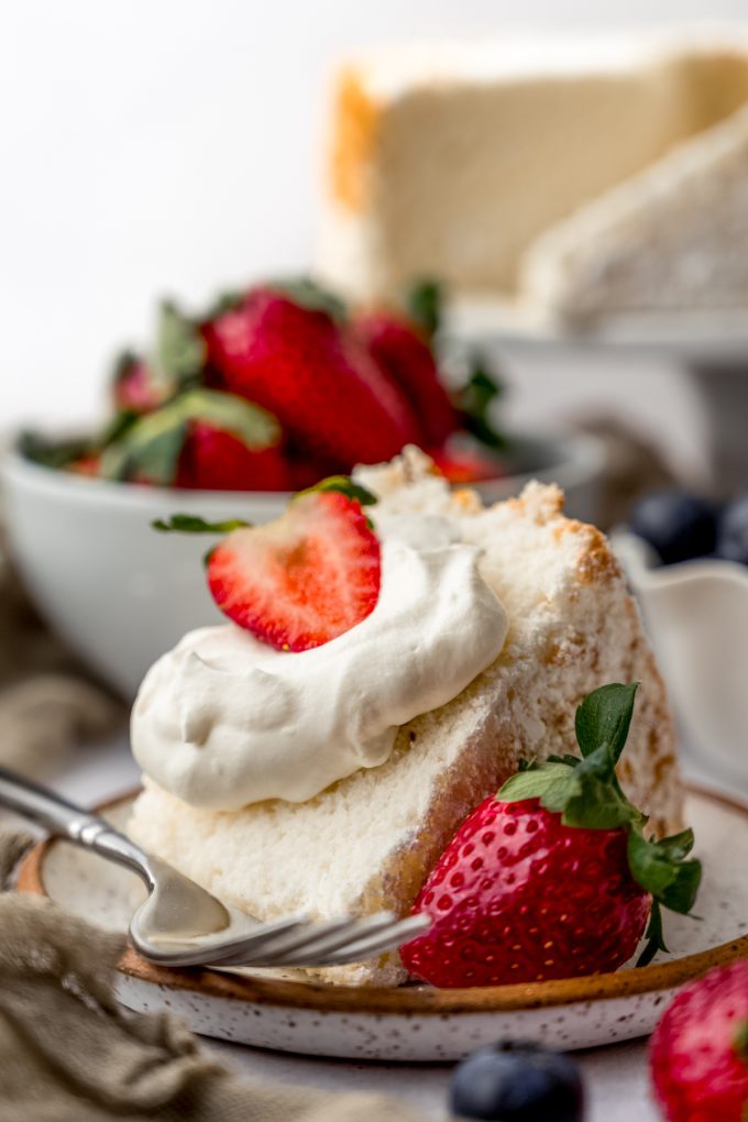 A slice of angel food cake with whipped cream and strawberries on it sitting on a plate with a fork.