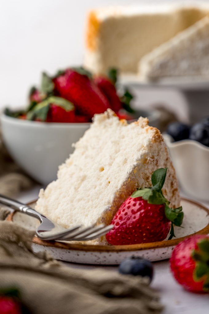 A slice of angel food cake sitting on a plate with a fork and a strawberry.