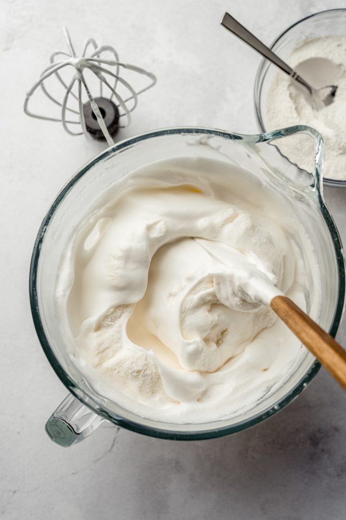 Aerial photo of angel food cake batter coming together in the bowl of a stand mixer with a spatula.