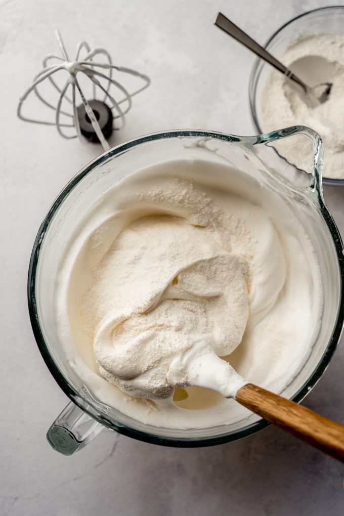 Aerial photo of angel food cake batter coming together in the bowl of a stand mixer with a spatula.