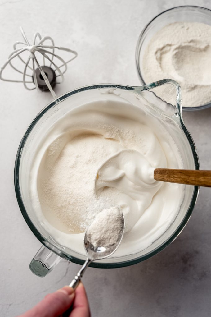 Someone is using a spoon to sprinkle the dry mixture onto the meringue portion of angel food cake.