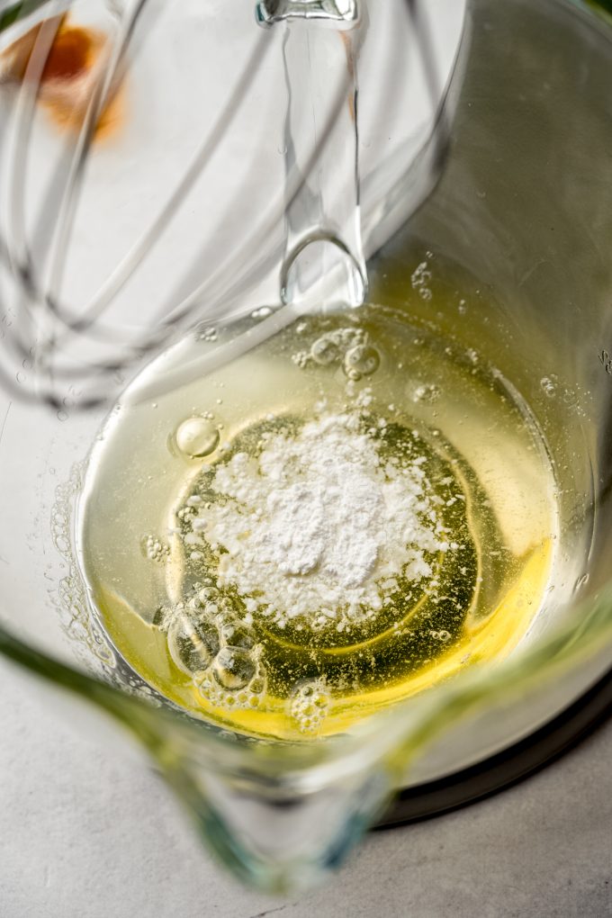 Egg whites and cream of tartar in the bowl of a stand mixer fitted with a whisk attachment.