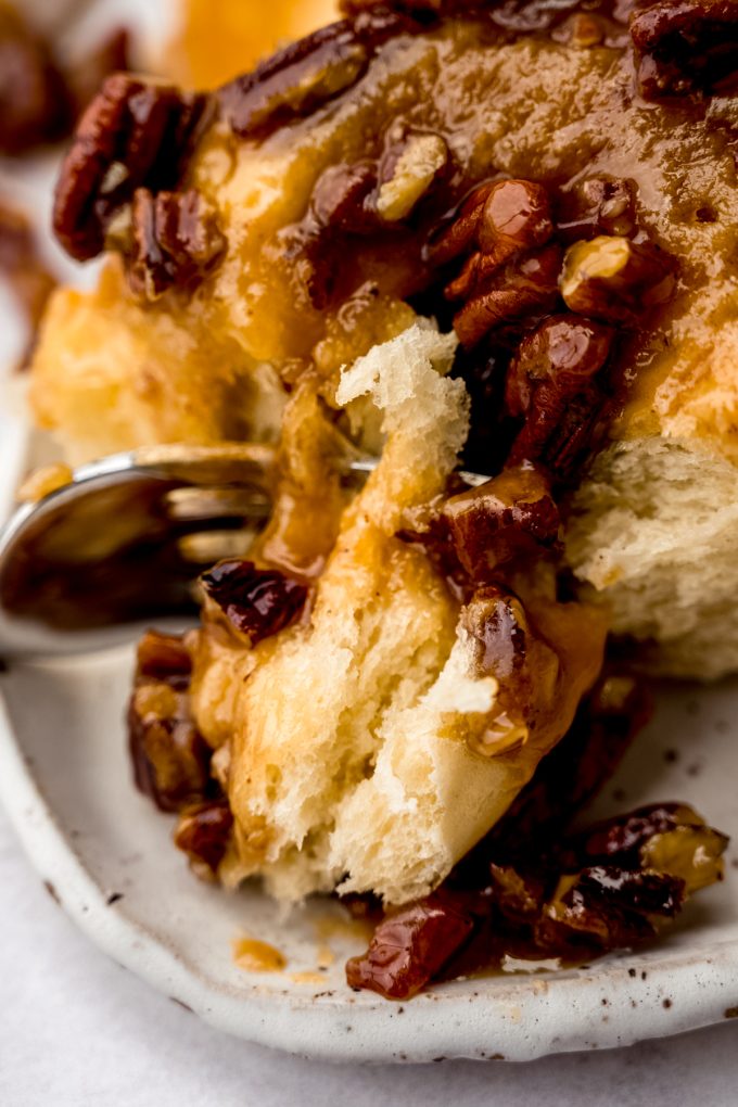 A sticky bun on a plate with a fork holding a bite of it.