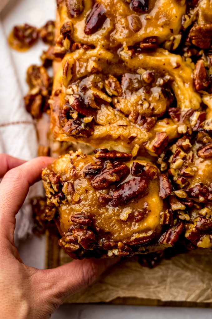 Someone's hand grabbing a sticky bun from a tray.