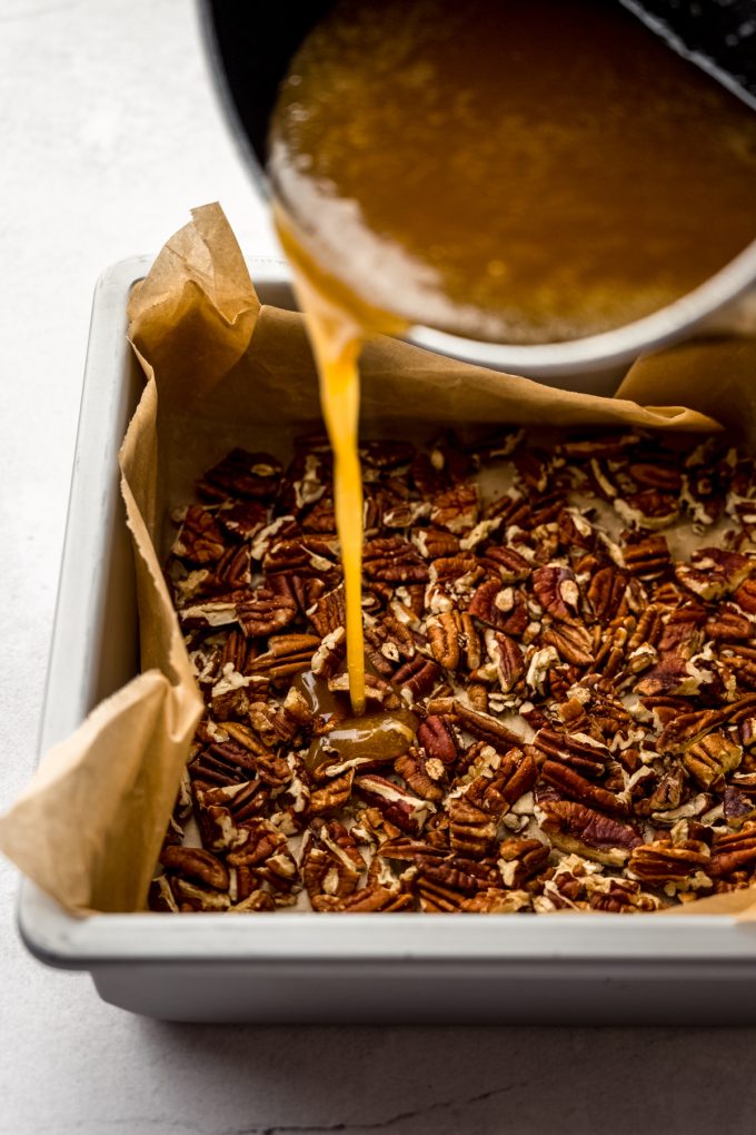 Someone is pouring maple caramel sauce into a pan lined with pecans to make sticky buns.