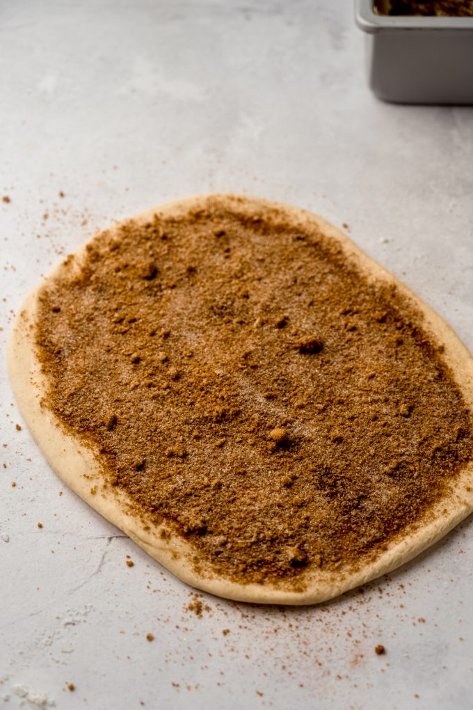 A rectangle of dough with cinnamon sugar on it ready to be rolled up into a log to make sticky buns.